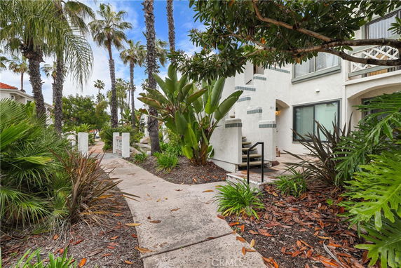 Pathway leading to a multi-story house with tropical plants and palm trees around.