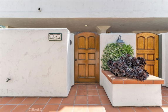 Front view of an entrance with wooden doors and white stucco walls.