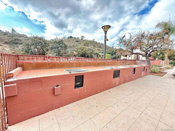 Outdoor paved area with red brick wall and lamppost, surrounded by trees and hills.