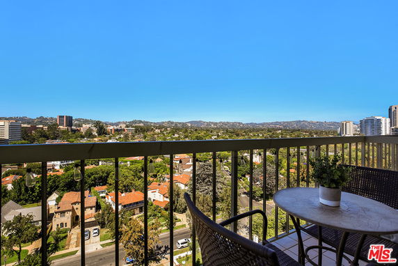 Wide-angle view from a balcony overlooking a cityscape with buildings and greenery.