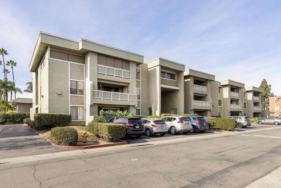 Front view of a multi-story apartment building with balconies and parking in front.