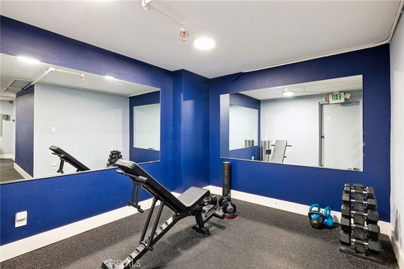 Indoor gym area with a weight bench, dumbbells, kettlebell, and large mirrors.