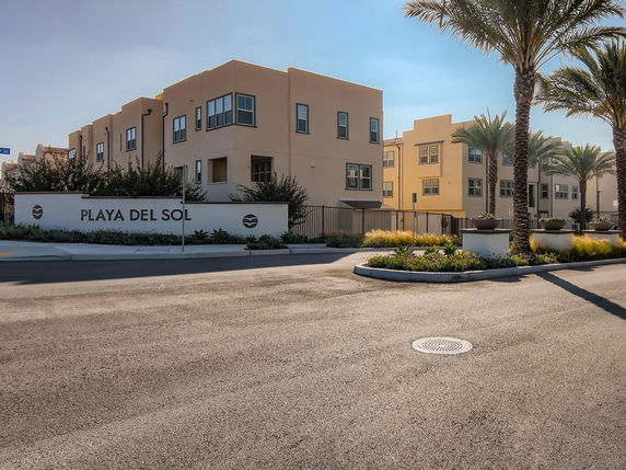 Front view of a multi-story building with large windows and palm trees in front.