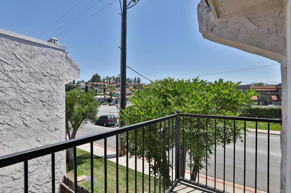 View from a balcony overlooking a street and nearby trees.