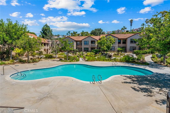 Outdoor swimming pool in front of residential buildings with landscaped surroundings.