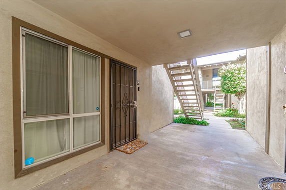 Exterior view of an apartment entrance with a security door and adjacent window, featuring a stairway leading to an upper level.
