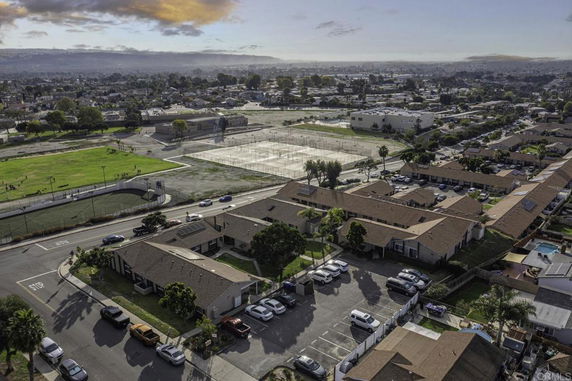 Aerial view of a residential area with streets and buildings, surrounded by greenery and distant hills.