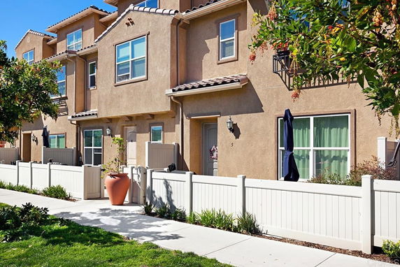 Front view of a multi-story house with a beige exterior and white fence.