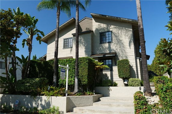 Front view of a multi-story house with a sloped roof and surrounding greenery.