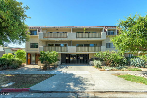 Front view of a multi-story apartment building with balconies and a gated parking entrance.