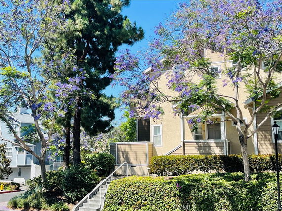 Front view of a multi-story house with a staircase leading to the entrance, surrounded by blooming trees.