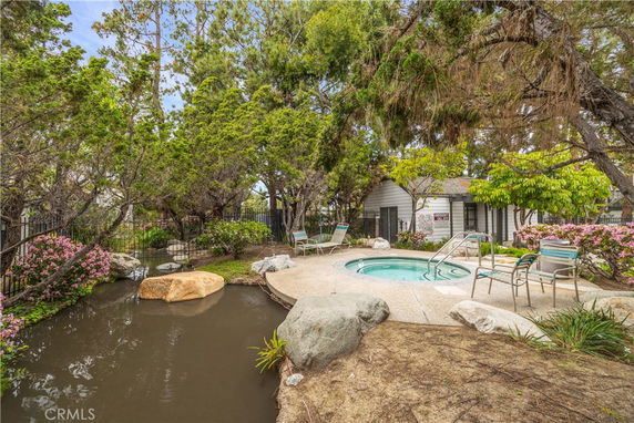 Outdoor area with a circular hot tub, surrounded by lounge chairs, trees, and foliage.