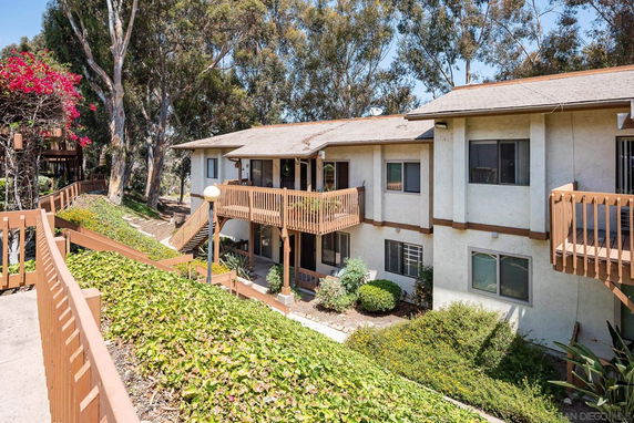Front view of a two-story apartment building with wooden balconies and surrounding greenery.