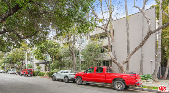 Front view of a multi-story apartment building with large windows and surrounded by trees.