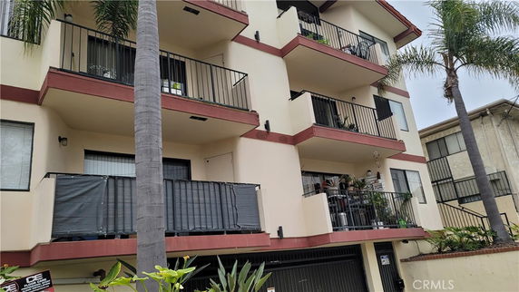 Front view of a multi-story residential building with balconies and palm trees.