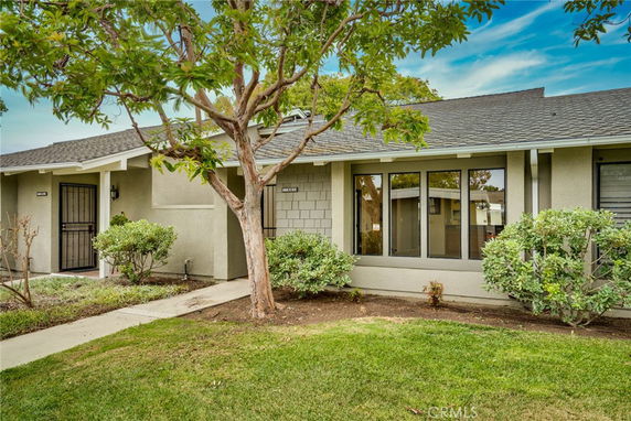 Front view of a single-story house with a tree and bushes.