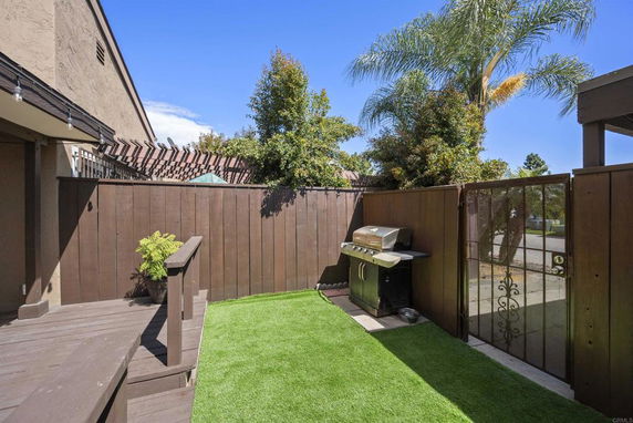 Outdoor area with artificial grass, a barbecue grill, and wooden fencing.