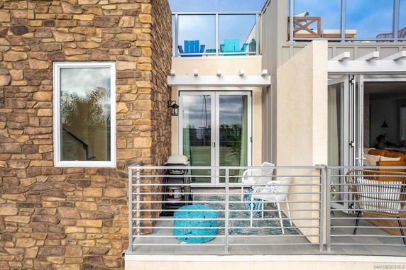 Front view of a modern house with stone and stucco exterior, featuring a small balcony with chairs and a table.