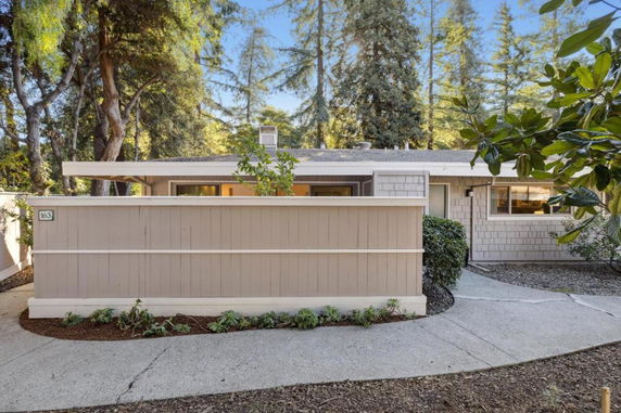 Front view of a single-story house with a low fence and surrounding trees.