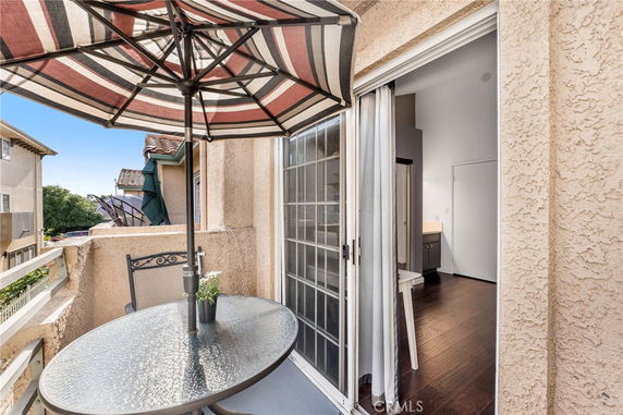 View from a small balcony with a round table and striped umbrella, overlooking neighboring buildings.