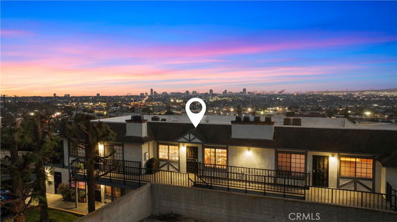 Panoramic view of a multi-story building with a city skyline in the background at sunset.