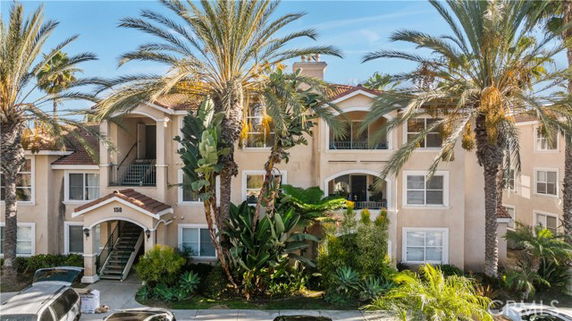 Front view of a multi-story residential building with a staircase entrance and surrounding palm trees.