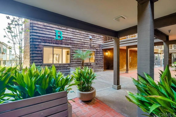 Covered outdoor area with letter 'B' on building wall and green plants.