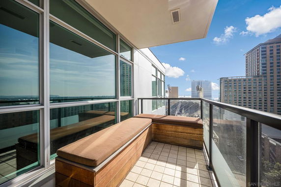 Rooftop balcony with glass railing offering a cityscape view including several high-rise buildings and a clear blue sky.