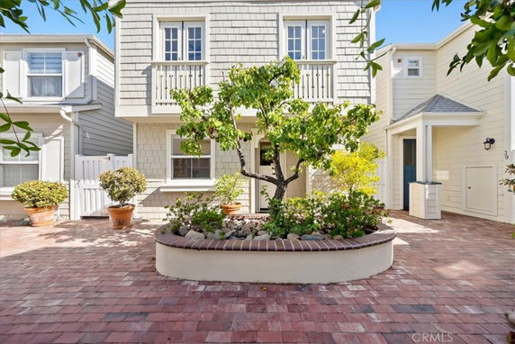 Front view of a two-story house with a small balcony and potted plants in a courtyard.
