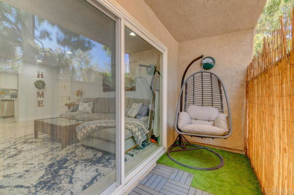 View of a balcony with a hanging chair and a glimpse of an indoor living space through a glass door.