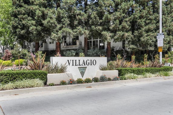 Front view of a residential complex with a sign reading 'Villagio' surrounded by trees and landscaping.