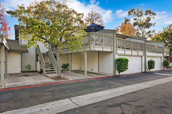 Front view of a residential building with a staircase leading to an upper deck and garages below.