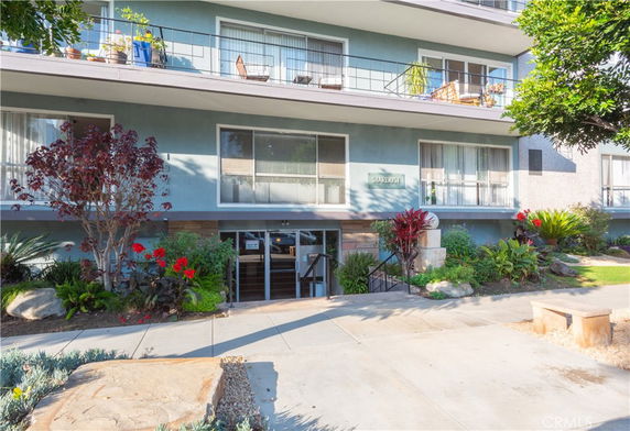 Front view of a multi-story residential building with balconies and landscaped entrance.