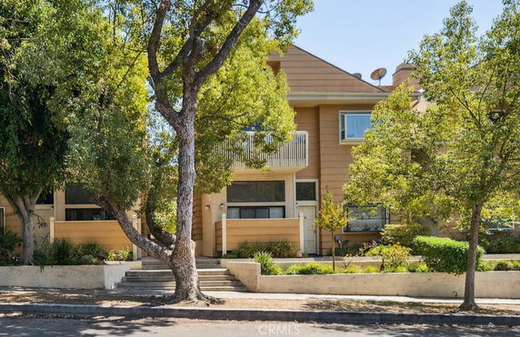 Front view of a two-story house with a balcony and surrounding trees.