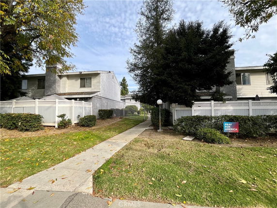 Front view of a two-story residential building with white fencing and a walkway leading to the entrance.