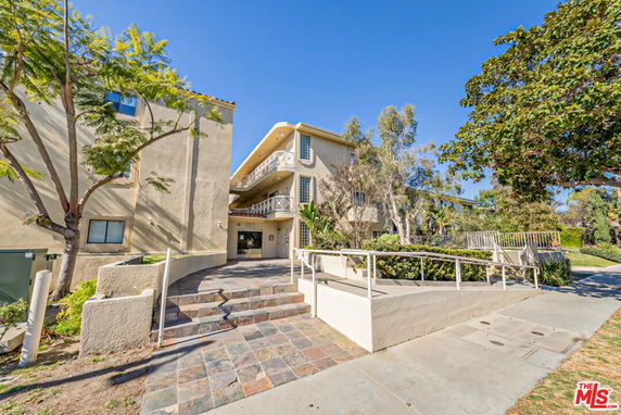 Front view of a multi-story residential building with balconies and stairs leading to the entrance.