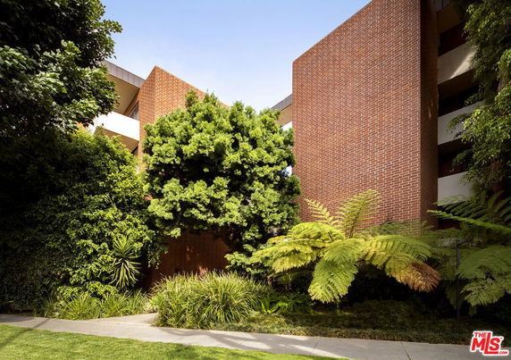 Front view of a multi-story brick building partially obscured by trees and plants.