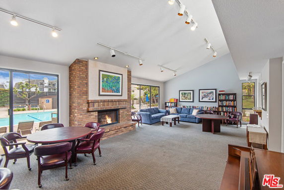 Interior of a clubhouse with seating areas, a brick fireplace, and large windows showing an outdoor pool.