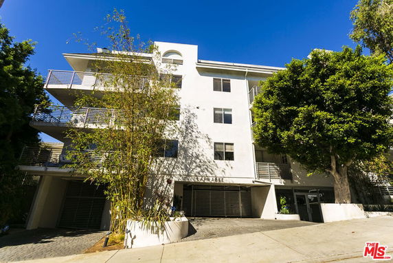 Front view of a multi-story apartment building with balconies and trees.