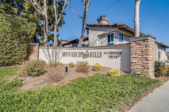 Front view of a residential building with a stone sign reading 'Monarch Hills', surrounded by greenery.