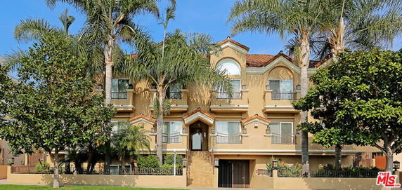 Front view of a multi-story building with balconies and palm trees.
