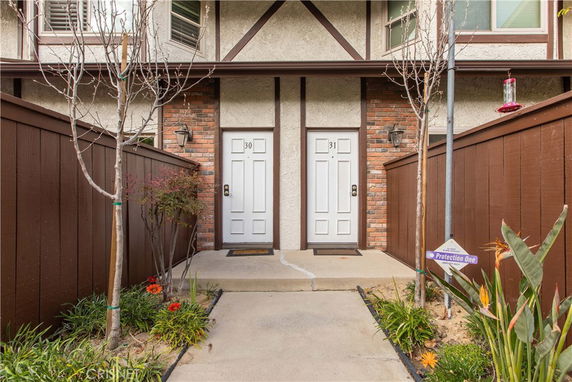 Front view of a multi-story building entrance with two doors marked 30 and 31, surrounded by a wooden fence and small garden.