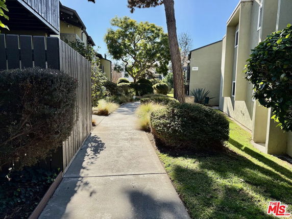Pathway between buildings with trees and shrubs.
