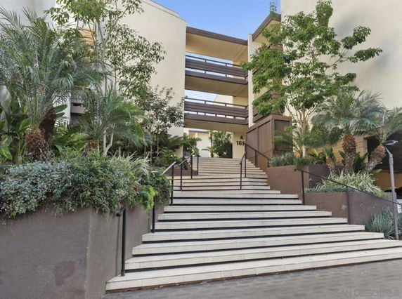Front view of a multi-story building with stairs and greenery.