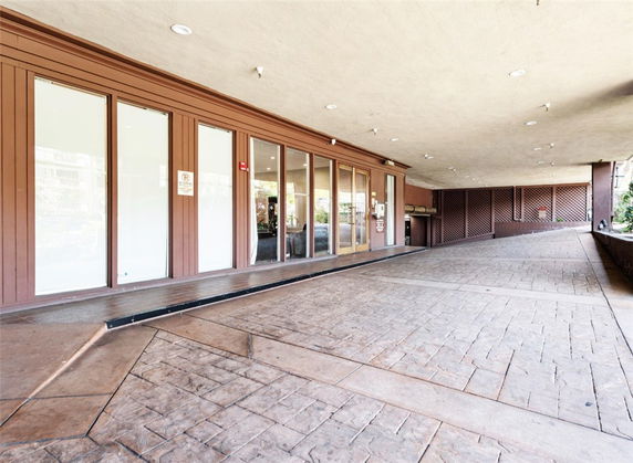 Covered parking area with a paved surface and glass-fronted building entrance.
