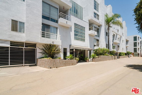 Front view of a modern multi-story apartment building with white exterior and several balconies.