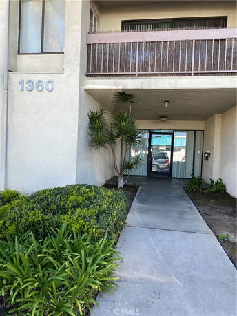 Front view of a building entrance with a pathway and overhanging balcony.