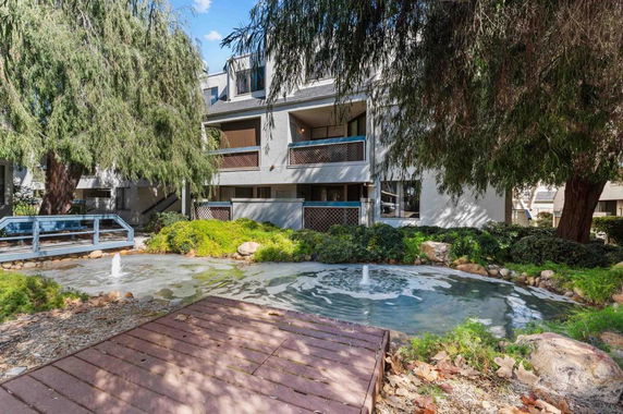 View of a multi-story building surrounded by trees and a small pond with a fountain.