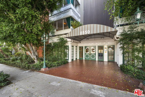 Front view of a building entrance with a striped awning and green double doors.