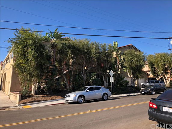 Front view of a multi-story building with trees partially obscuring the structure and several cars parked on the street.